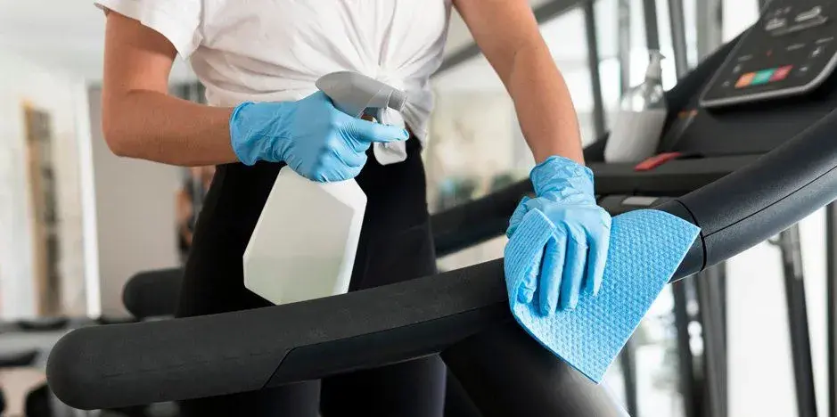 Professional+cleaner+wearing+gloves+wiping+gym+equipment-1920w